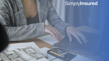 Female is typing on a laptop with calculator, paperwork, and small pile of money.