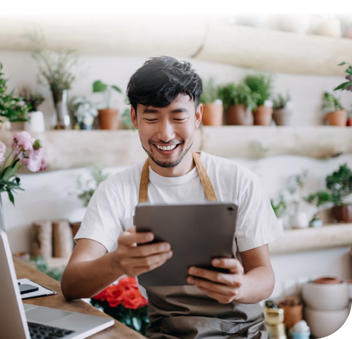 Man standing in front of plants, smiling at tablet